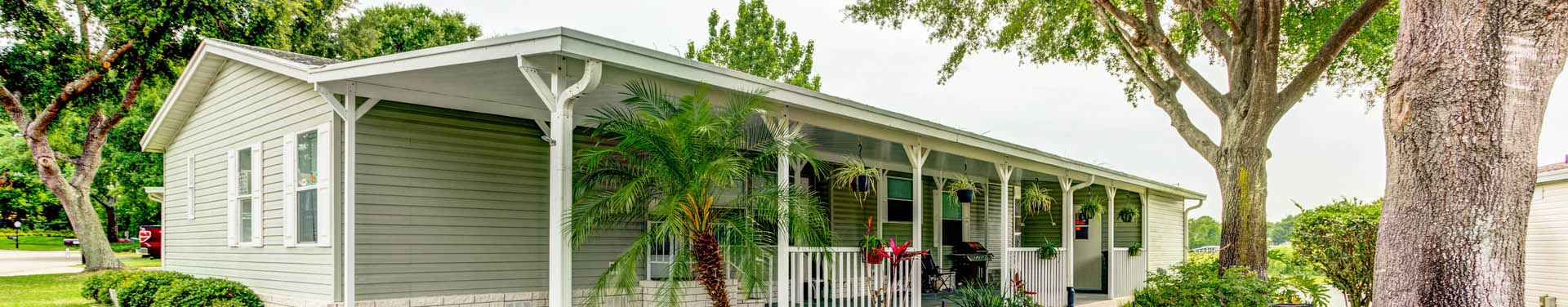 Photo of a mobile home with a nice front porch and greenish siding, surrounded by trees